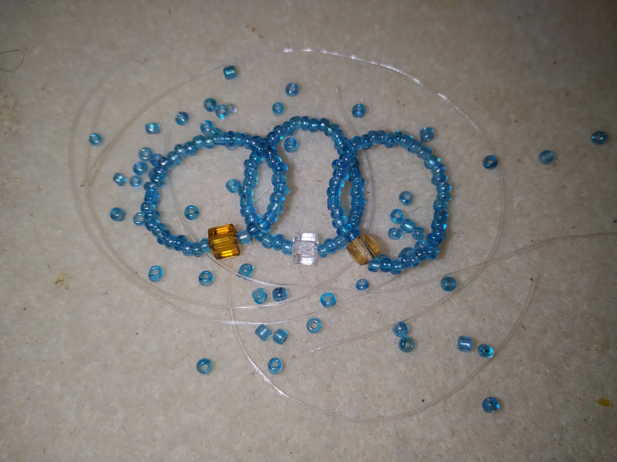 Blue Trinity Blessing Bands with three accent stones representing the Father, Son, and Holy Spirit, displayed on a neutral surface with scattered blue beads