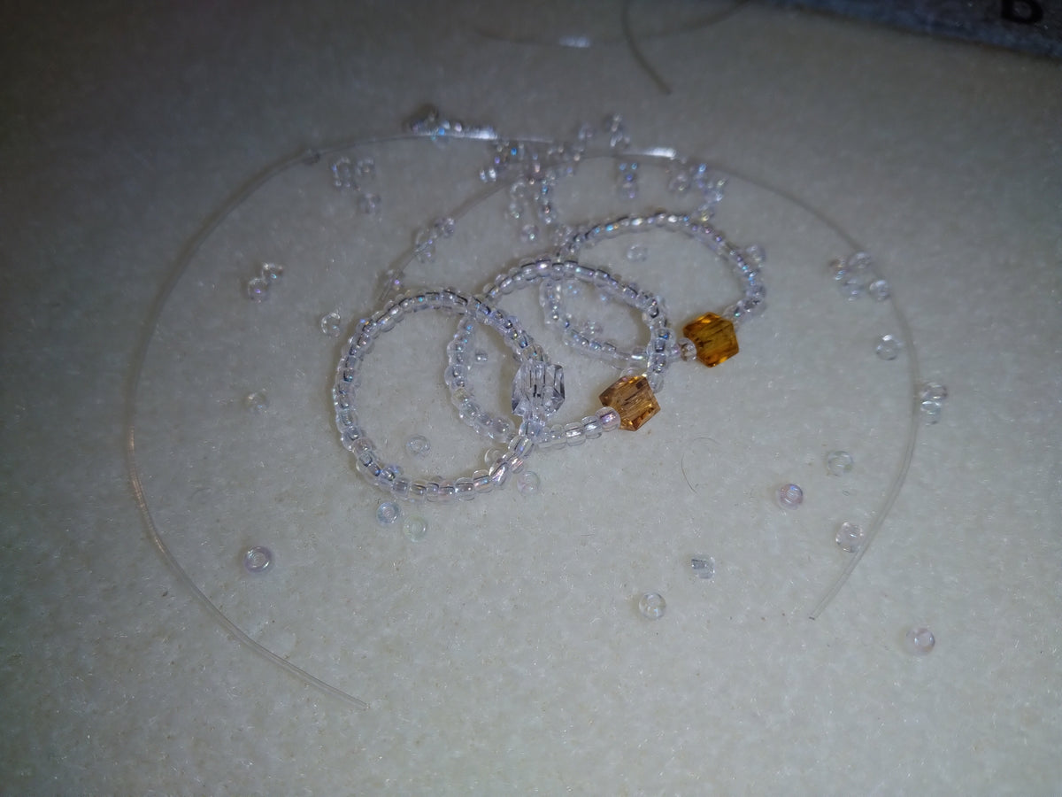 Clear Trinity Blessing Bands with three accent stones representing the Father, Son, and Holy Spirit, photographed on a neutral surface with scattered clear beads