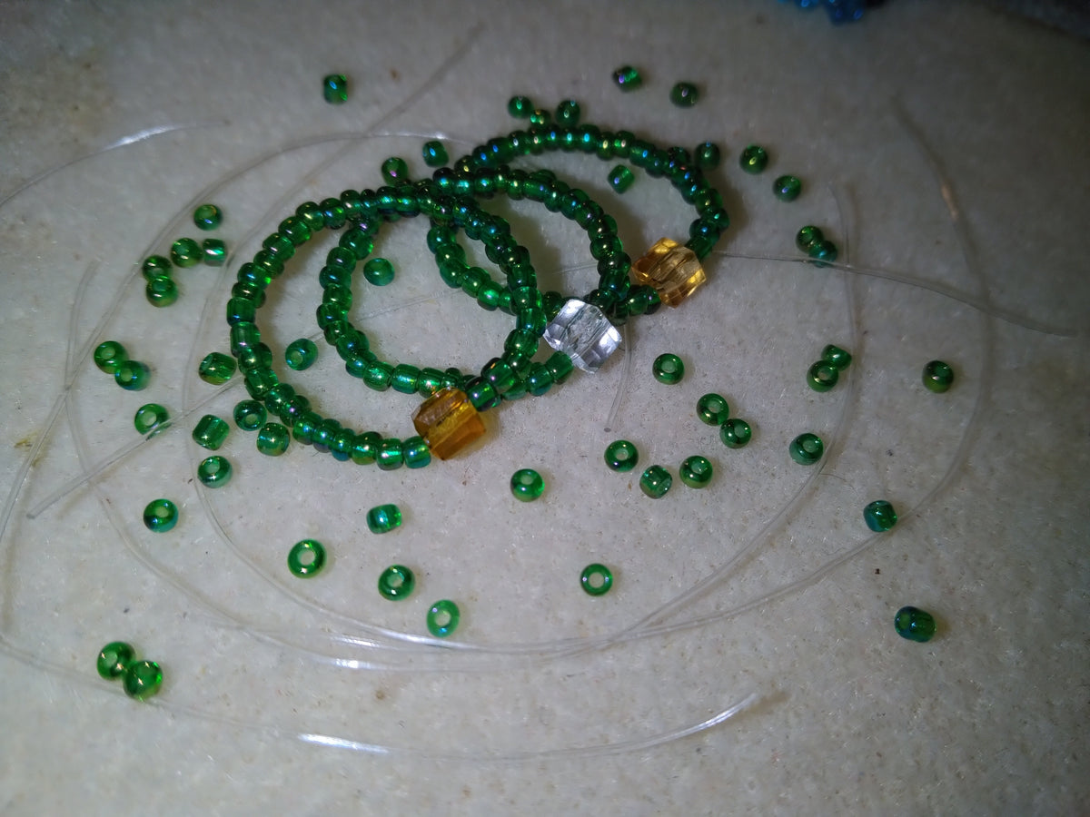 Green Trinity Blessing Bands with three accent stones representing the Father, Son, and Holy Spirit, displayed on a neutral surface with scattered green beads